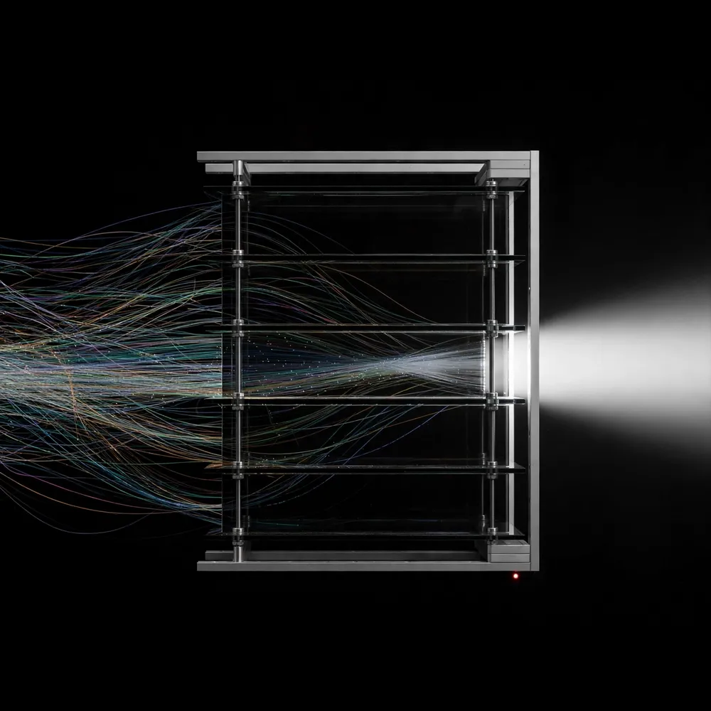 Many tangled threads of light enter a stack of dark glass panes and leave as a single clean beam.